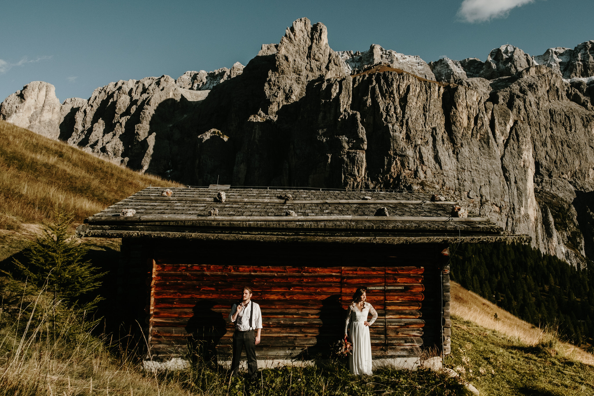 Planning a wedding in the alps - image of a bride and groom in front of a wooden mountain hut in the Italian Alps by Wild Connections Photography
