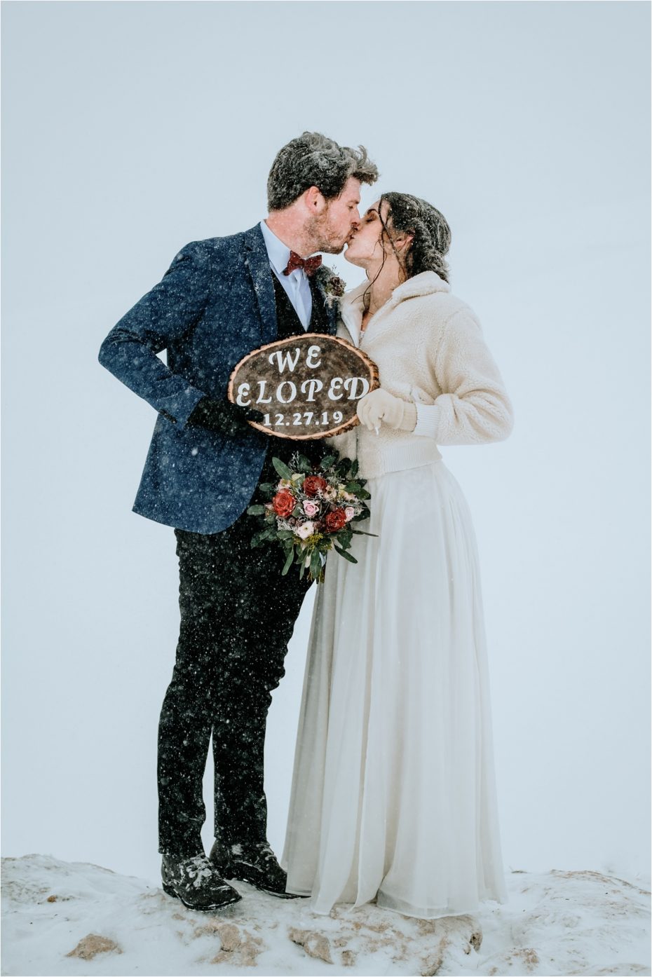 Bride and groom hold a sign that says "we eloped" as they kiss in the snow. The perfect detail to mark the occasion.