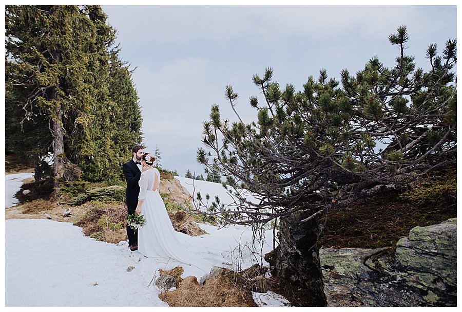 Honeymoon shoot in Austria Groom kisses bride on the forehead as they stand in the snow on top of a mountain by Wild Connections Photography
