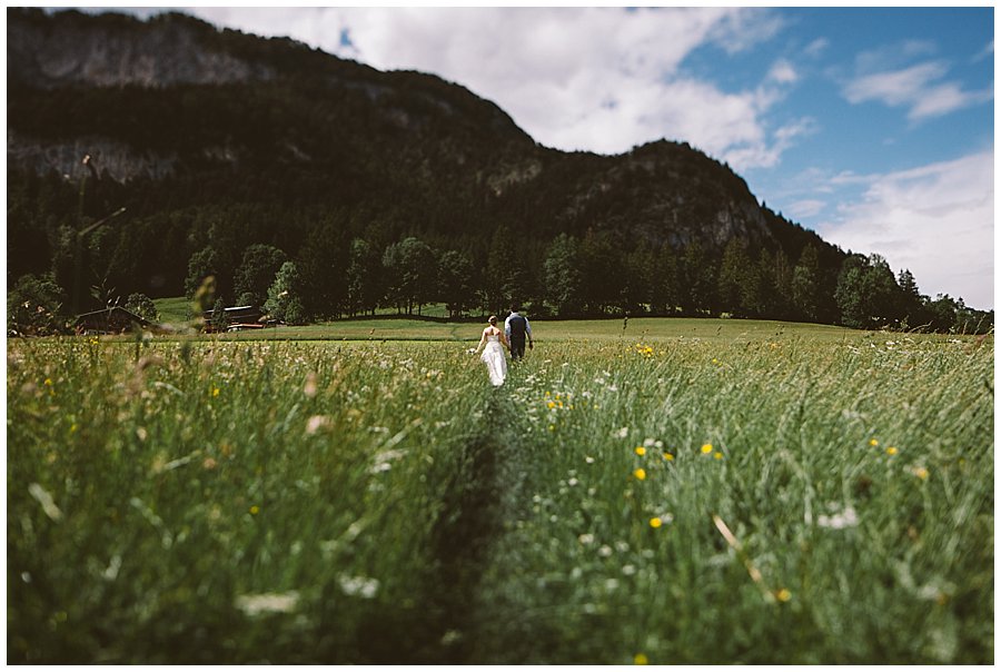 Couple walking away through long grass in Austria with mountain backdrop photo by WIld Connections Photography