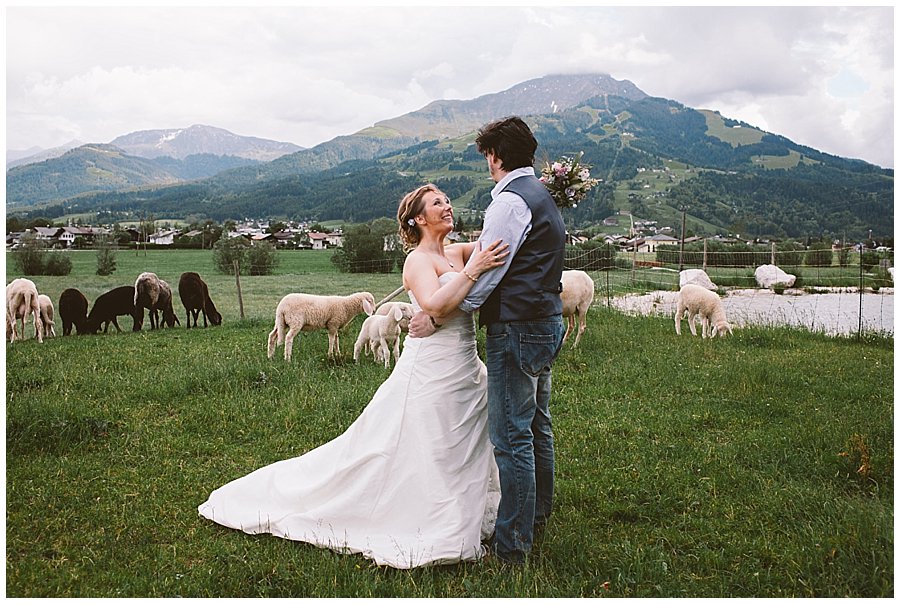 St Johann in Tirol Elopement Nikki and Chris stand in a field of sheep with mountains behind them by Wild Connections Photography
