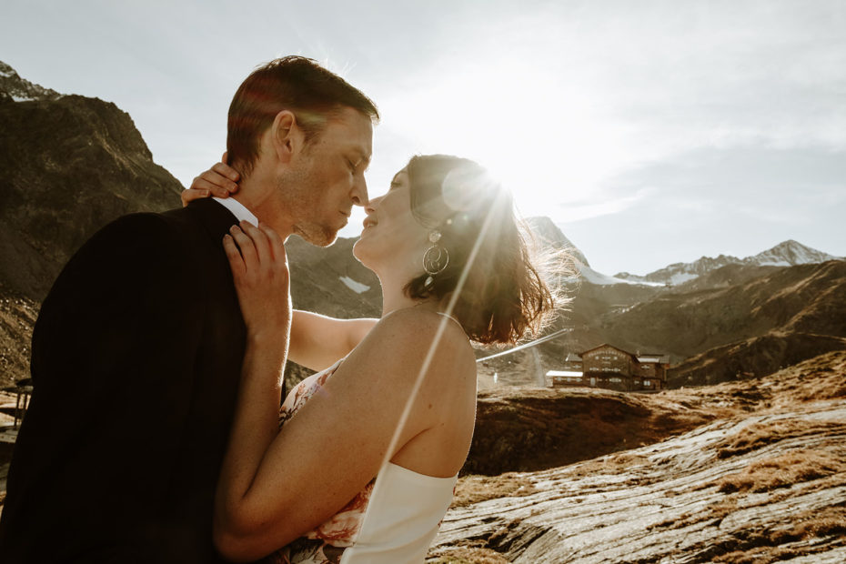 Bride and groom in the foreground with a mountain hut in the background behind them
