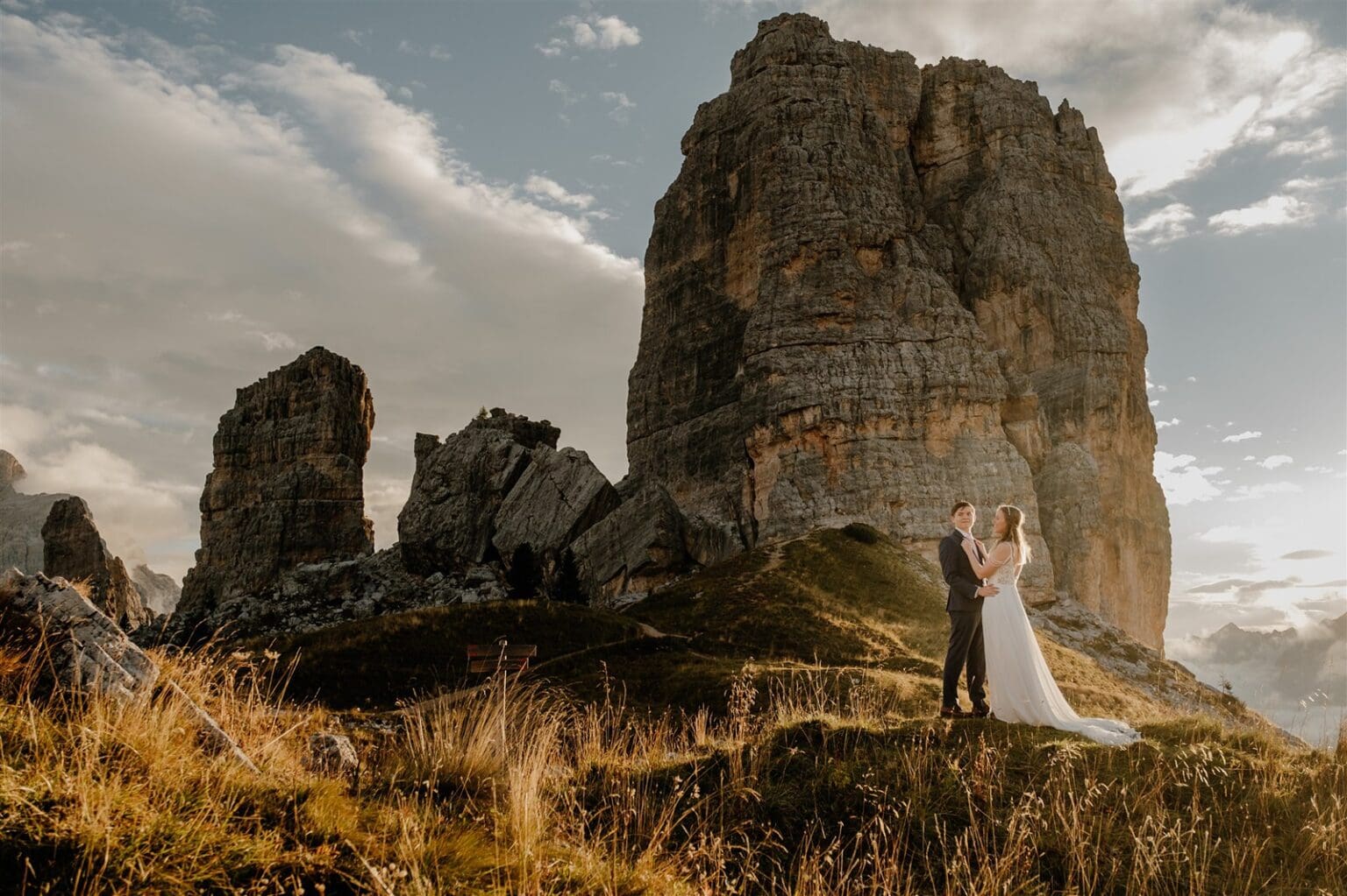 Bride and groom stand on a rock at sunrise in front of the Cinque Torri 5 towers in the Dolomites in Italy