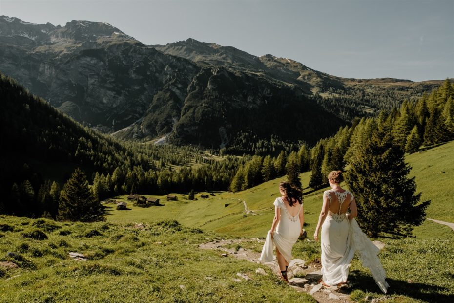 two brides hiking down a mountain meadow trail after their adventure elopement in the Austrian Alps