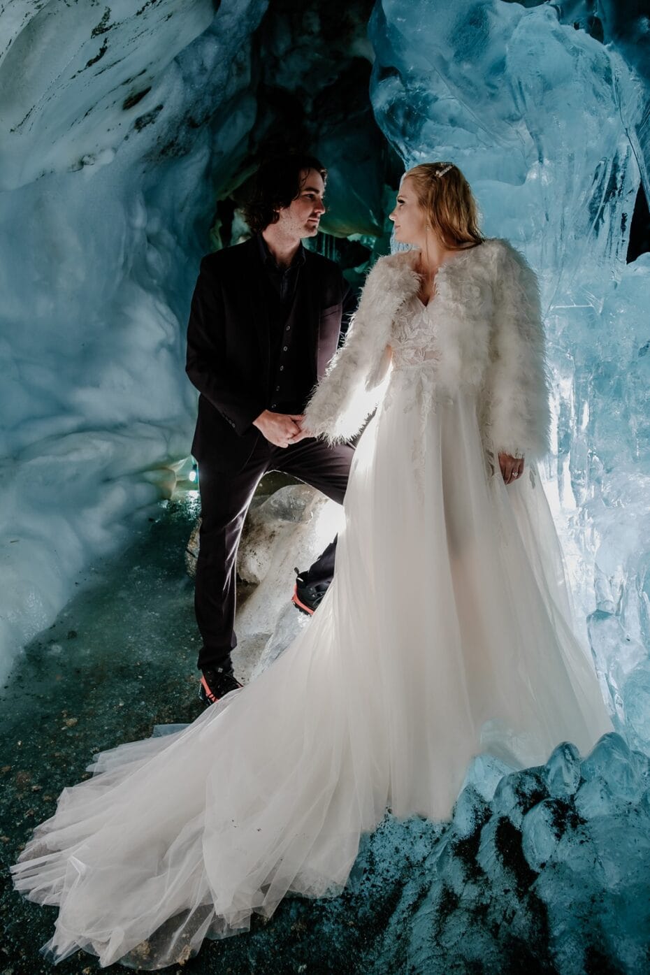 Bride and groom hold hands inside an ice cave on a glacier in the Austrian Alps