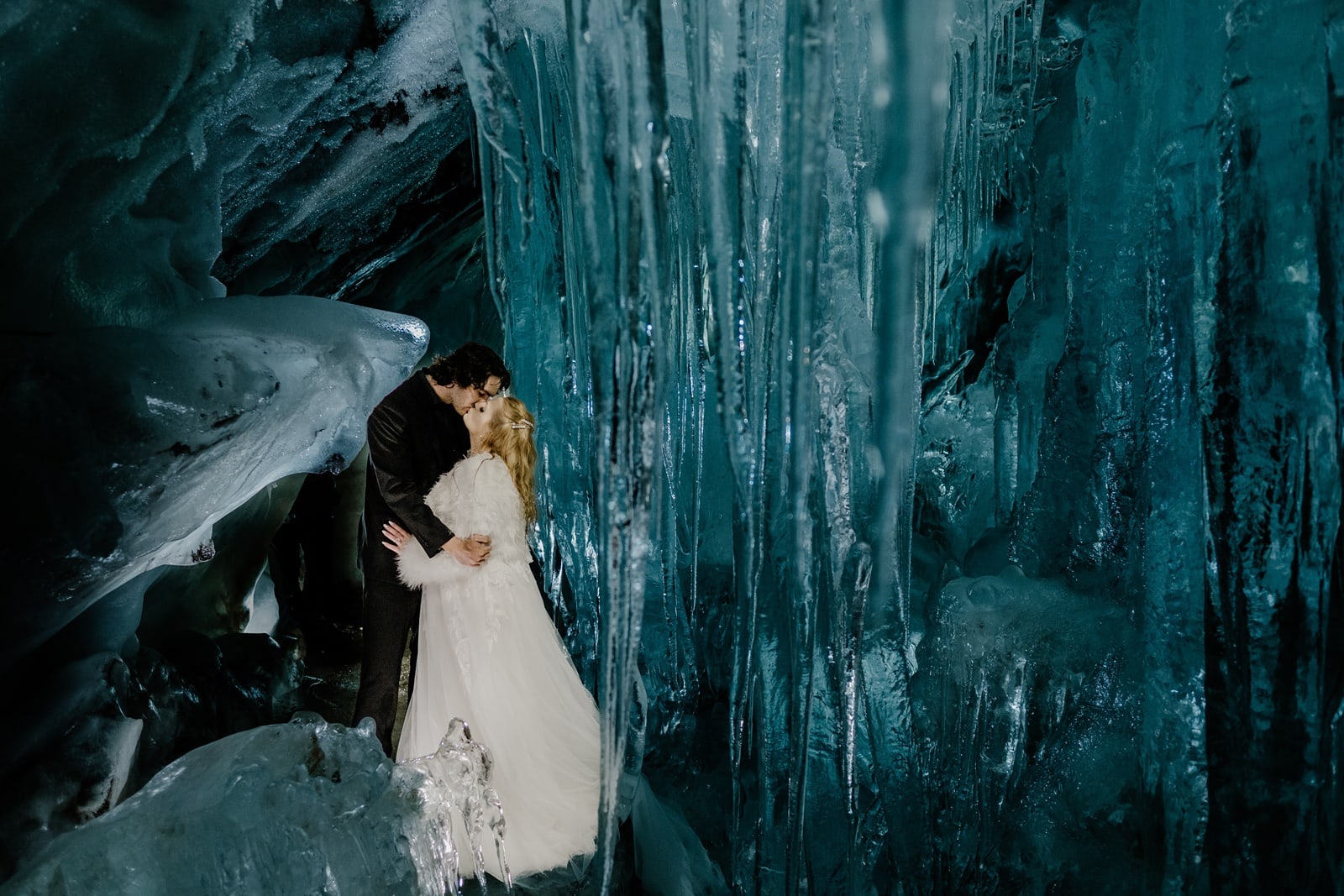 Bride and groom kiss inside a glacier ice cave