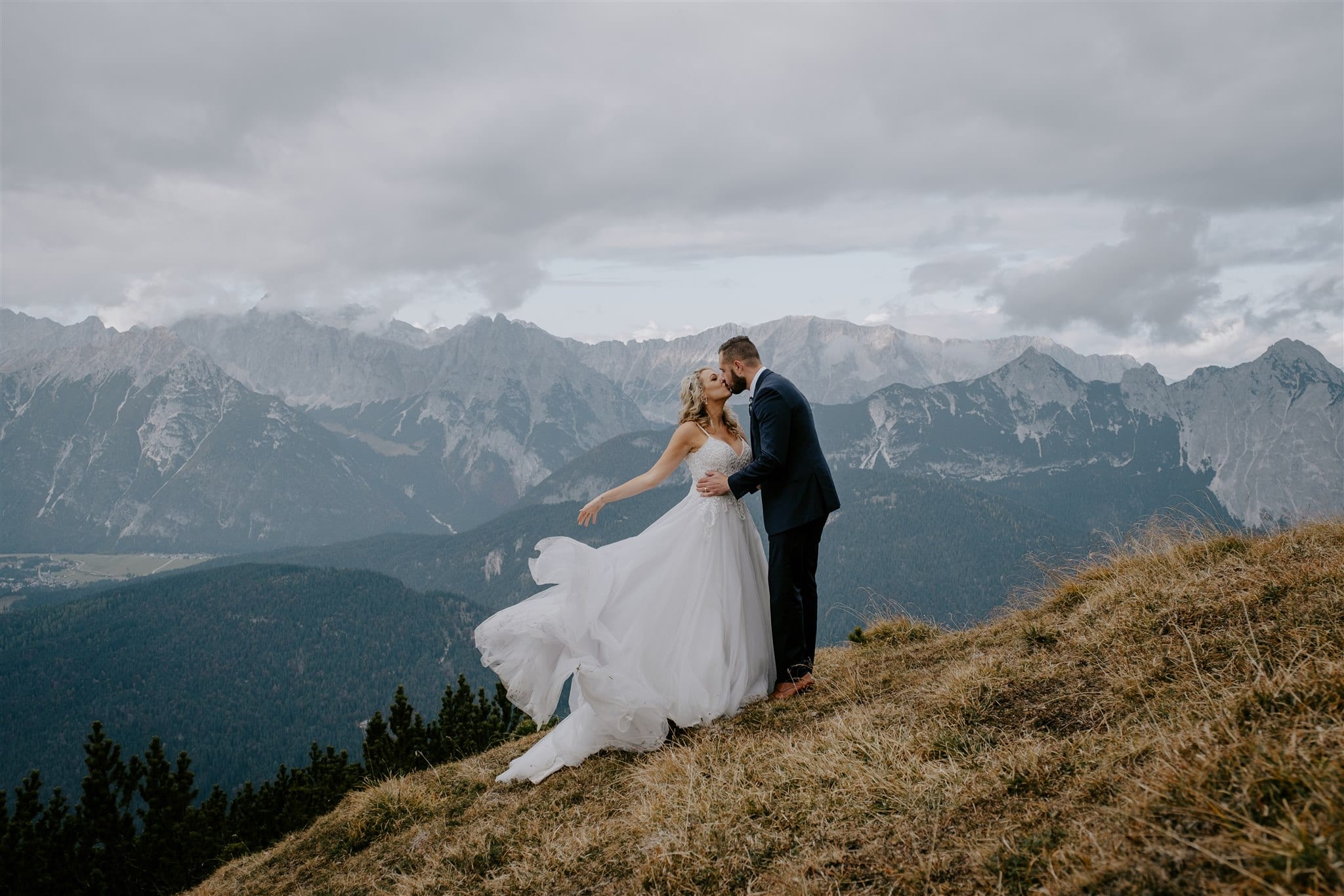 An elopement in Tirol, the bride and groom kiss on the top of a mountain as the dress blows in the wind