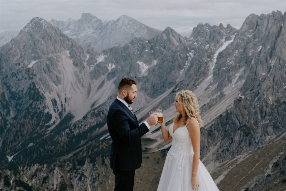 Bride and groom toast their elopement wedding in Tyrol by sharing a beer on the top of the Seefelderspitze