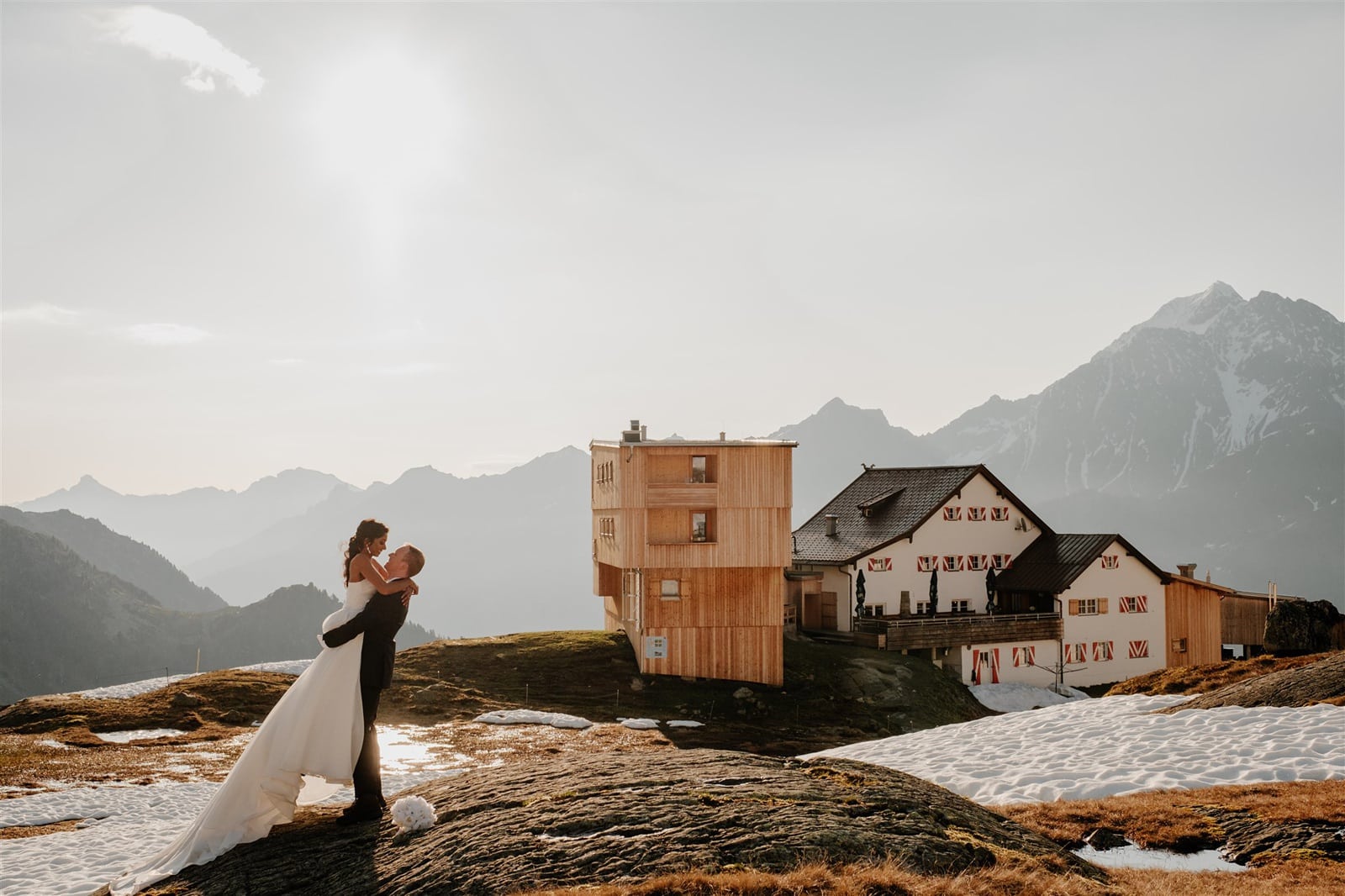 Bride and groom embrace in front of a mountain hut in the Austrian Alps