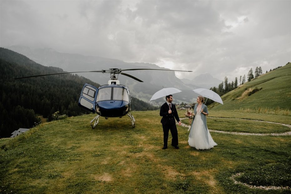 Couple return from helicopter wedding in the Dolomites in the rain holding umbrellas