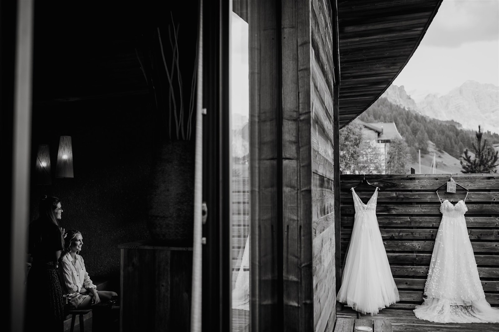 Two wedding dresses hang on a wooden fence with the Dolomites mountains in the distance behind them