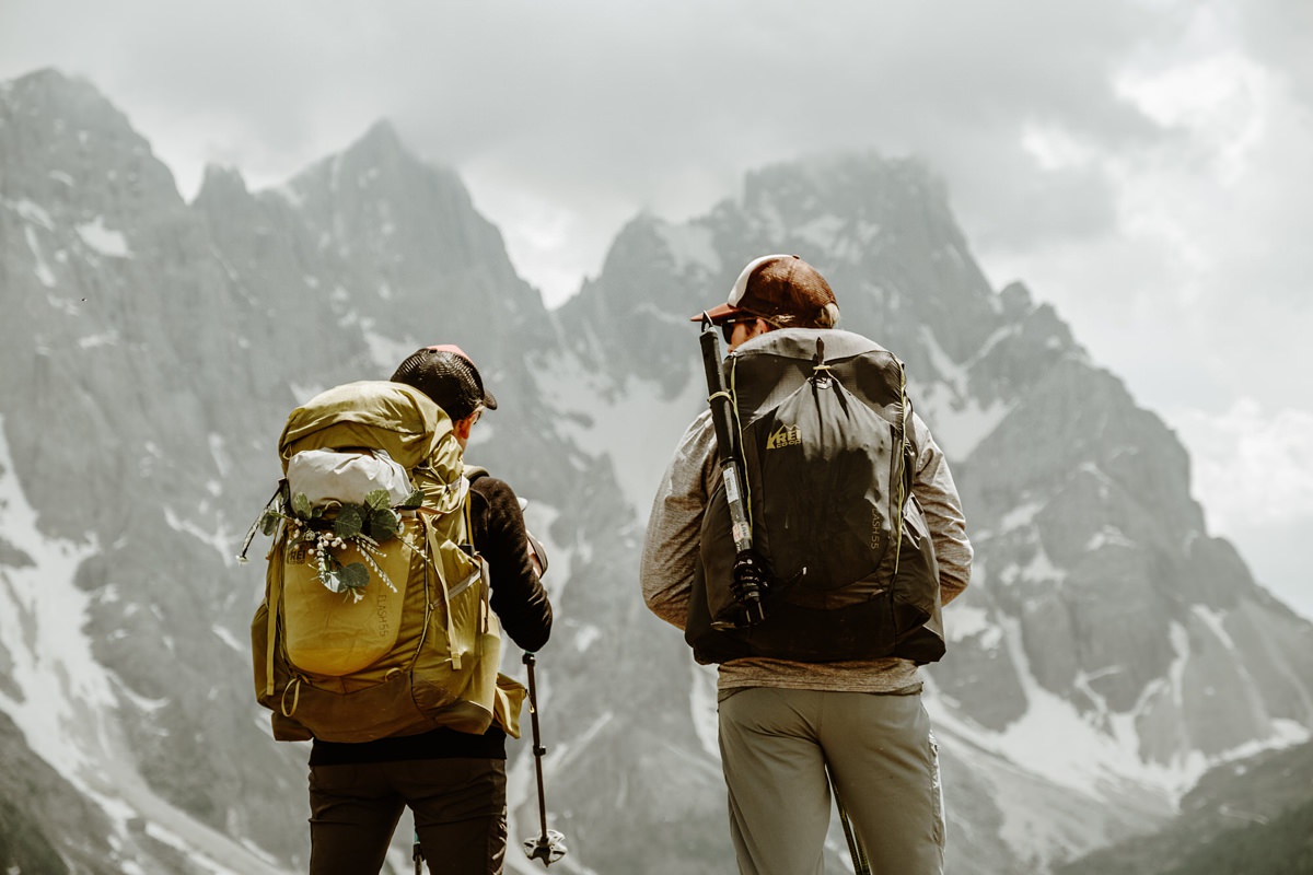 A man & a woman with backpacks facing into the distance looking at the mountains