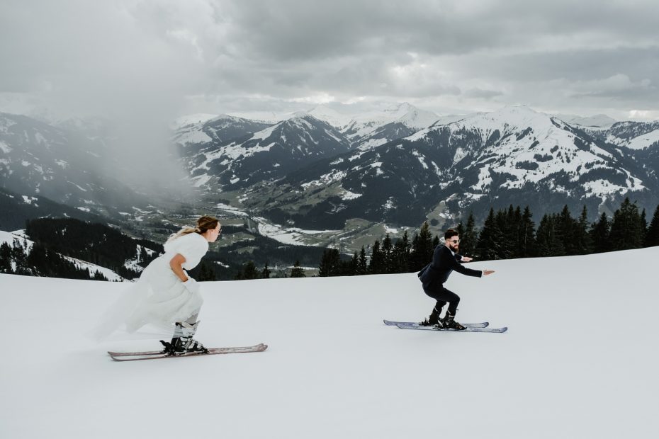 Bride and groom racing down a ski slope on skis on their wedding day