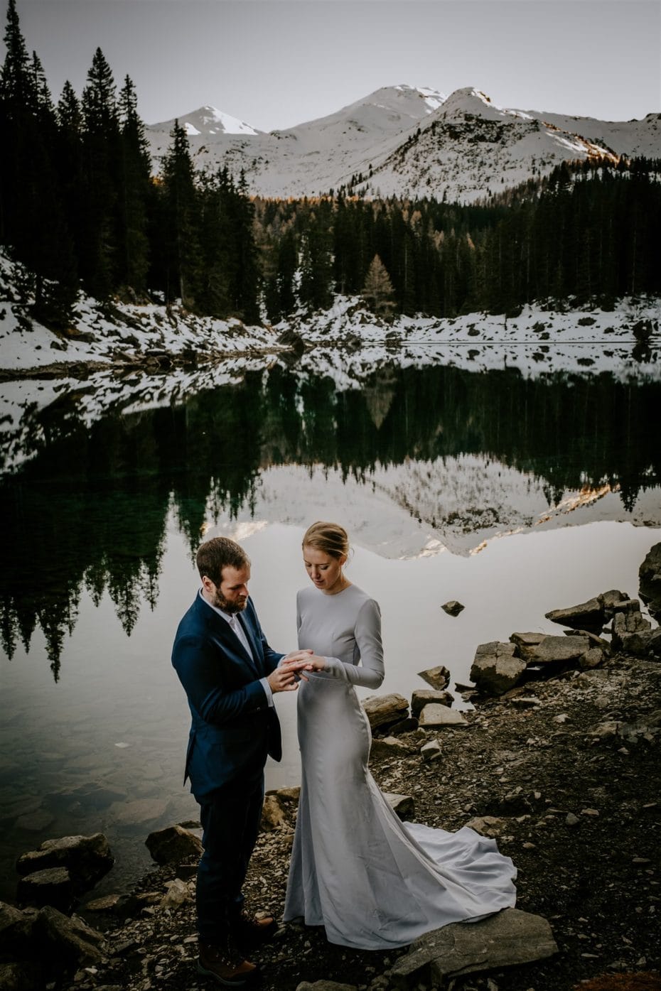 Winter mountain elopement in Innsbruck Austria, bride and groom exchange rings by a lake with snow capped mountains in the distance