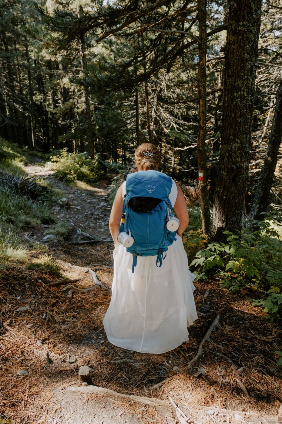 Bride hiking in a wedding dress with a blue Osprey backpack