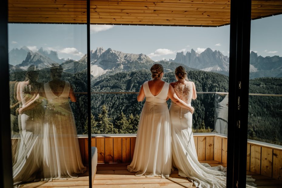 Two brides stand on the balcony of Forestis hotel in the Dolomites