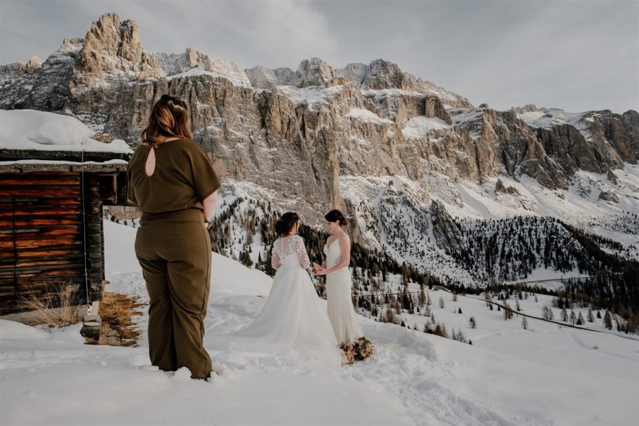 Two brides read their wedding vows to one another against a snowy mountain backdrop in the Dolomites