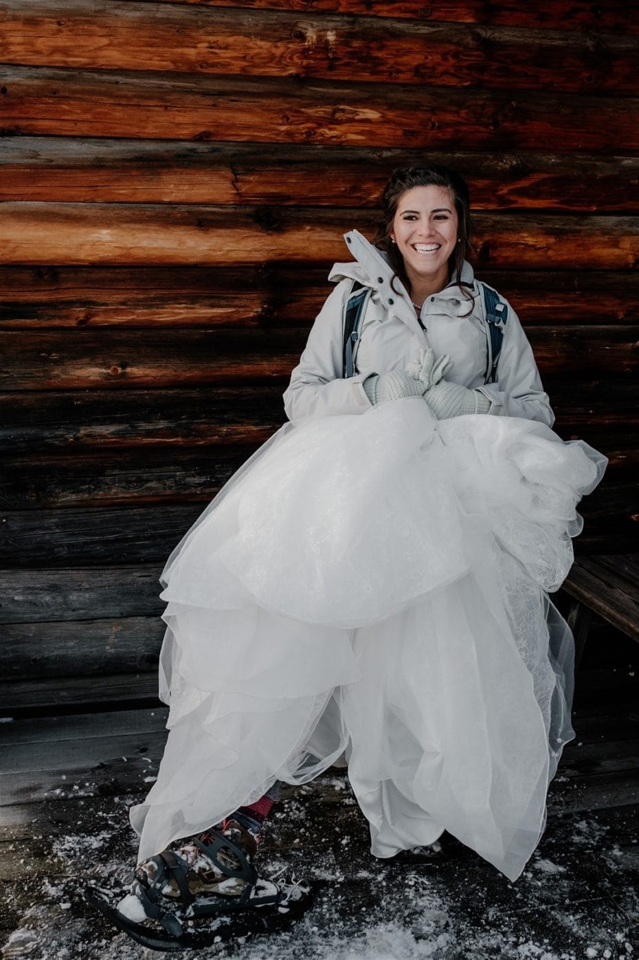 A smiling bride wearing a ski jacket, wedding dress and snowshoes