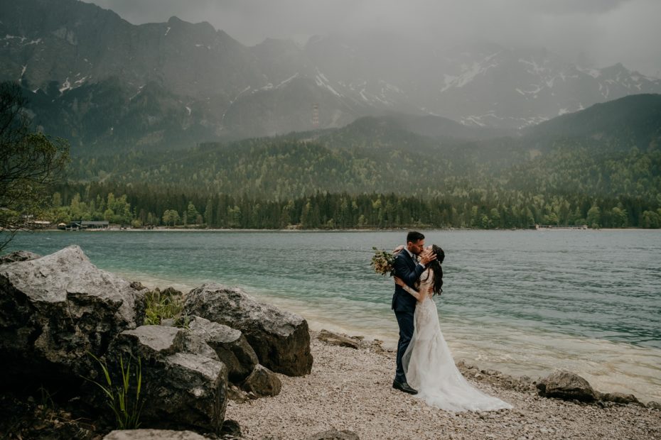 Bride and groom kiss in the rain on the shore of lake Eibsee in Germany