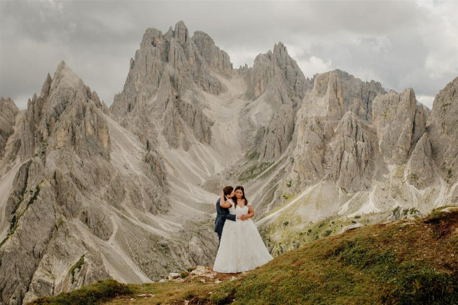 Bride and groom embrace in front of the jagged mountain peaks of Cadini di Misurina in the Dolomites