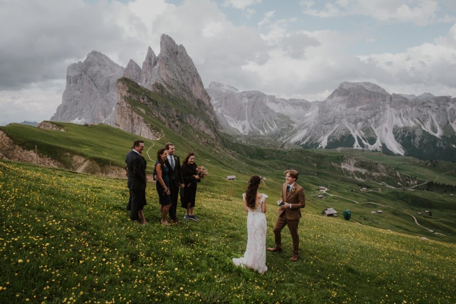 A small group of people stand on the edge of the Seceda ridgeline on the Dolomites in Italy for an elopement wedding ceremony by helicopter