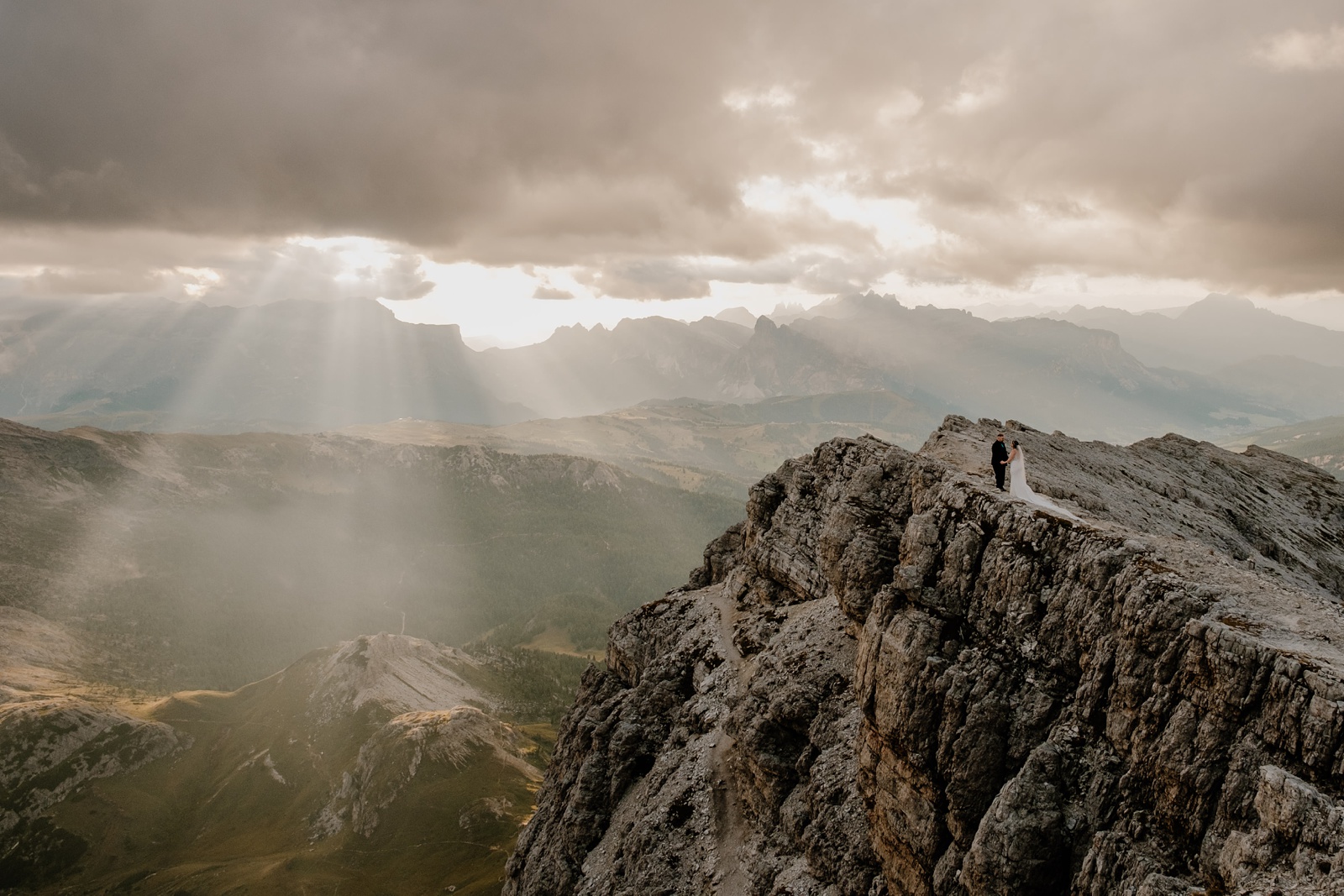 A sunset mountain hut elopement with a bride and groom standing on a cliff edge as the sun is setting behind them.