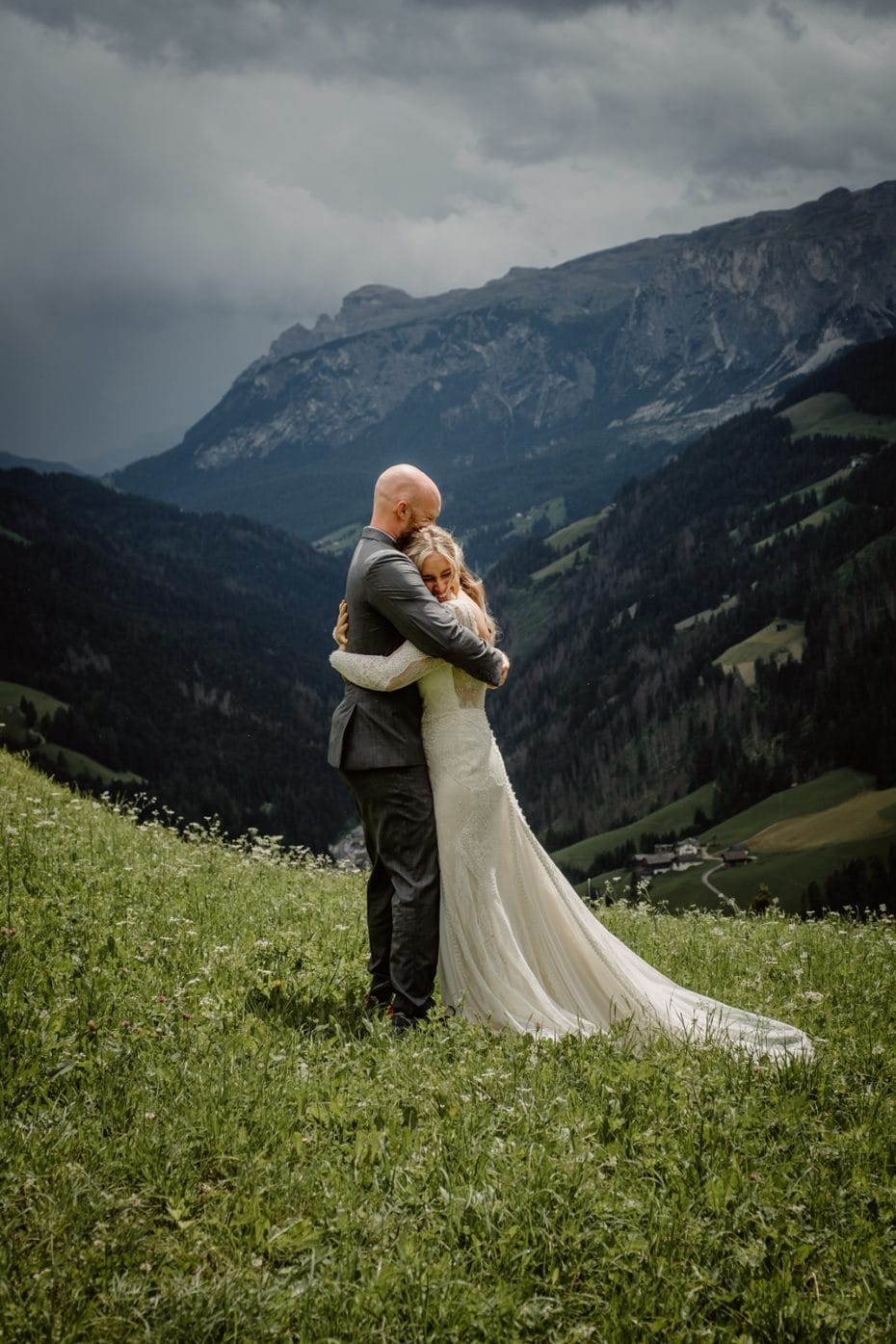 Bride and groom embrace tightly with dark clouds and mountains in the distance