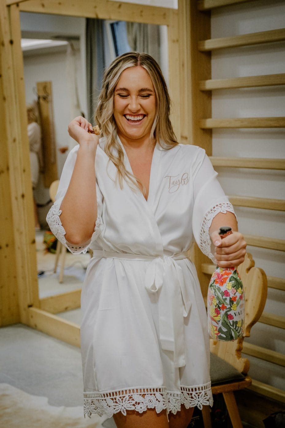 Bride pops bottle of champagne while wearing silk robe
